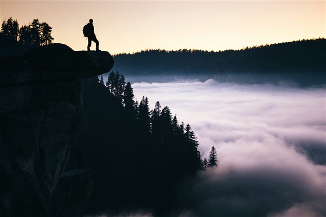 photo d'une personne en haut d'un rocher qui examine le brouillard, symbolisant une personne qui déteste son travail et cherche les causes